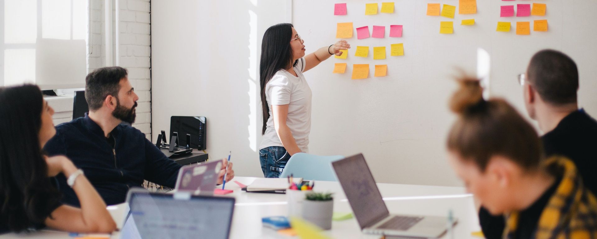 Imagen de alumna frente a pares mostrando trabajo de análisis con post-its en pizzarra blanca.