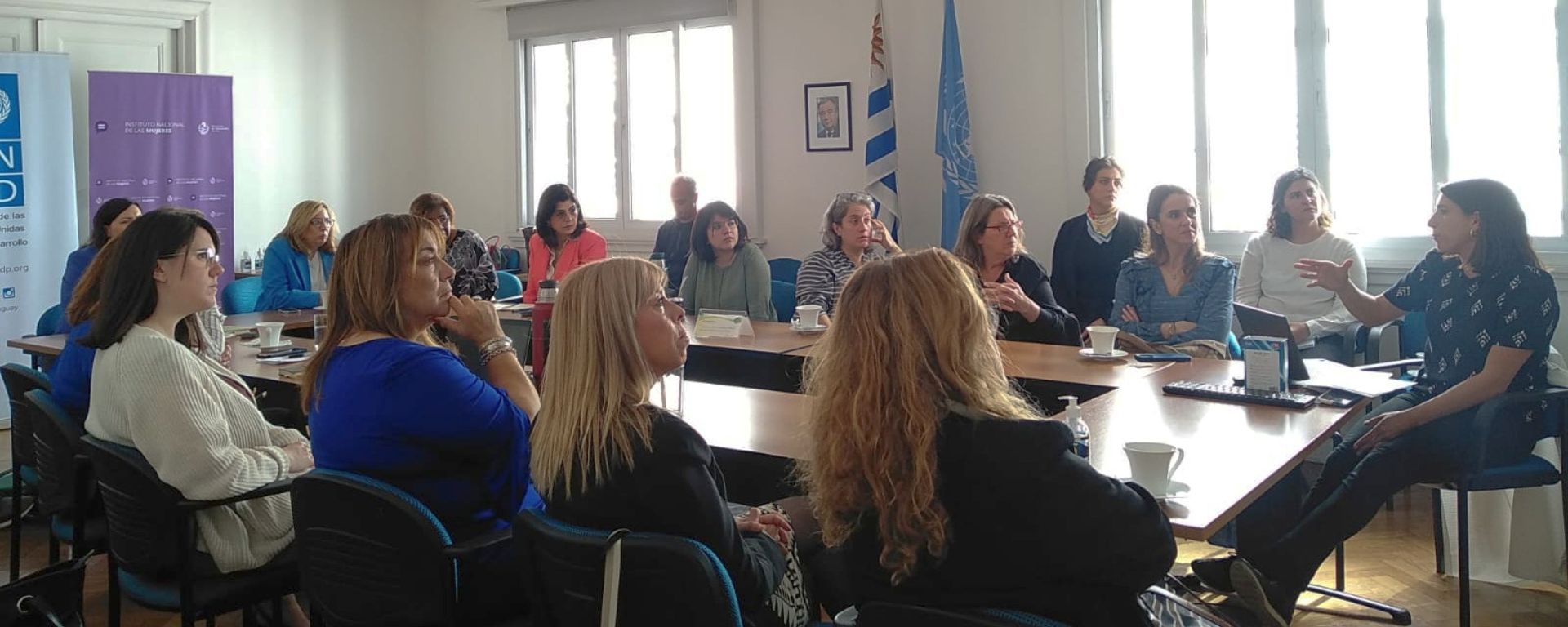 Mujeres participantes sentadas alrededor de una mesa grande en escuchan a una referente.