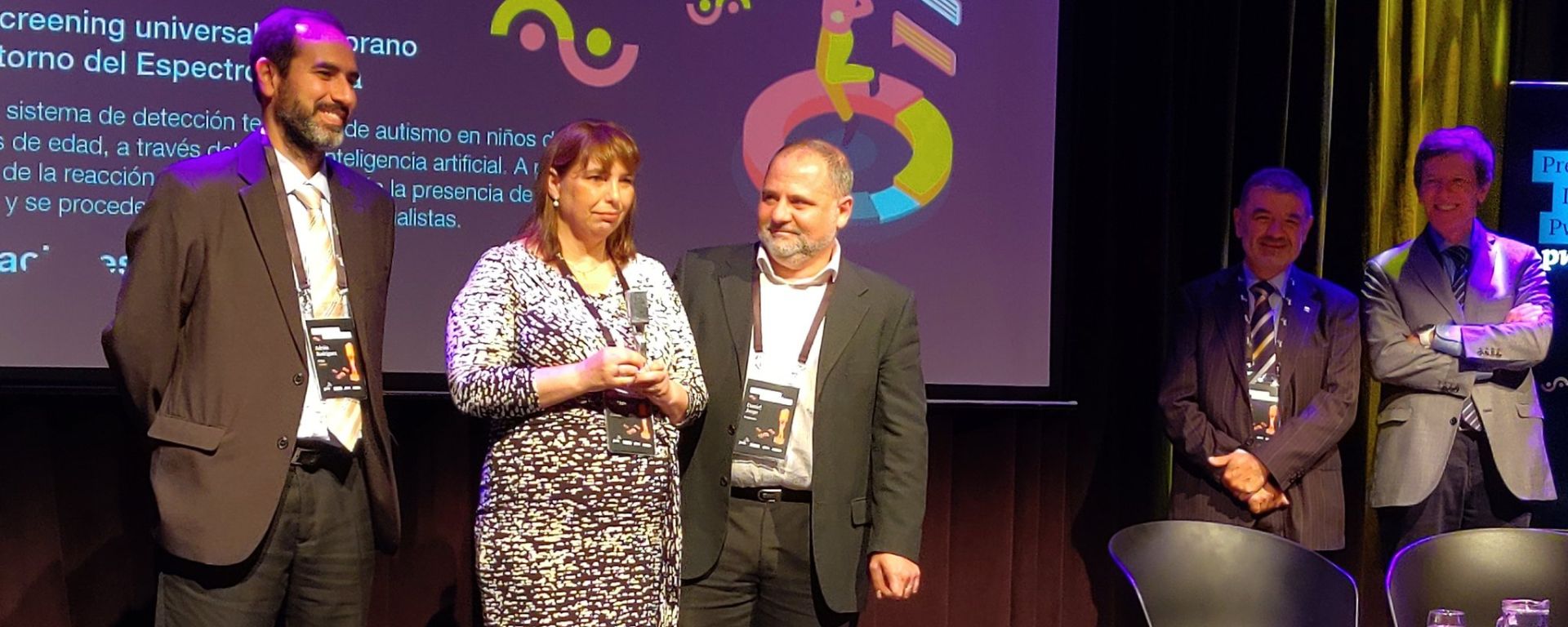 Docente UM recibe premio en escenario, junto a colega